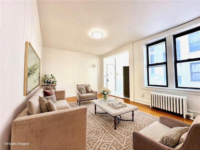 living area with a decorative wall, radiator, baseboards, and light wood finished floors