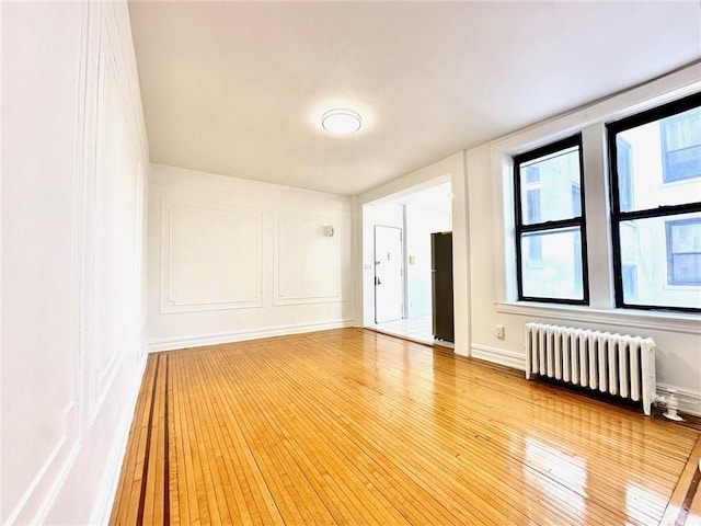 empty room featuring a decorative wall, radiator heating unit, baseboards, and hardwood / wood-style floors