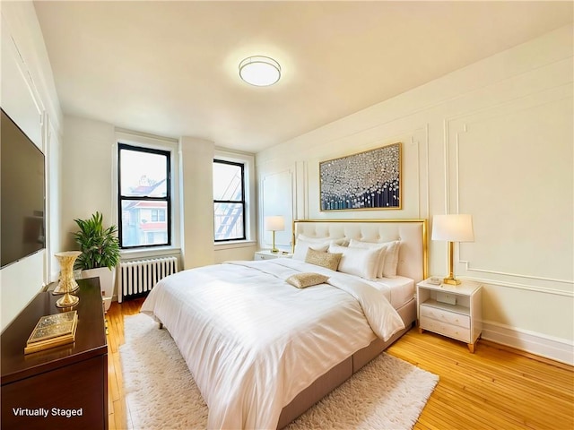 bedroom featuring light wood-style floors, radiator, and a decorative wall