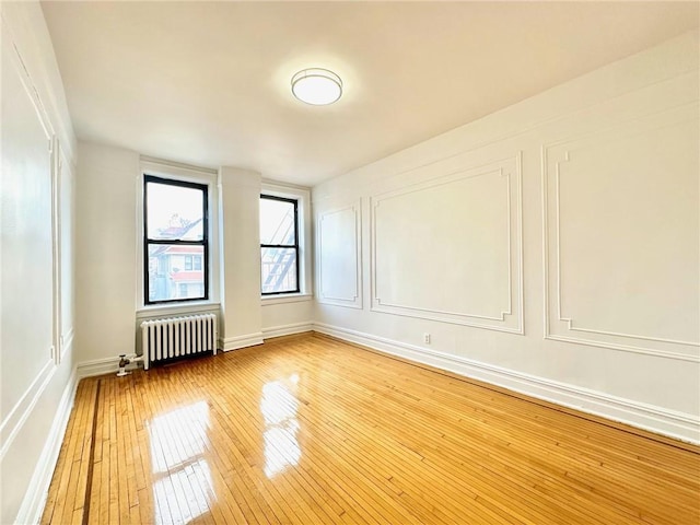 spare room with a decorative wall, radiator heating unit, and hardwood / wood-style floors