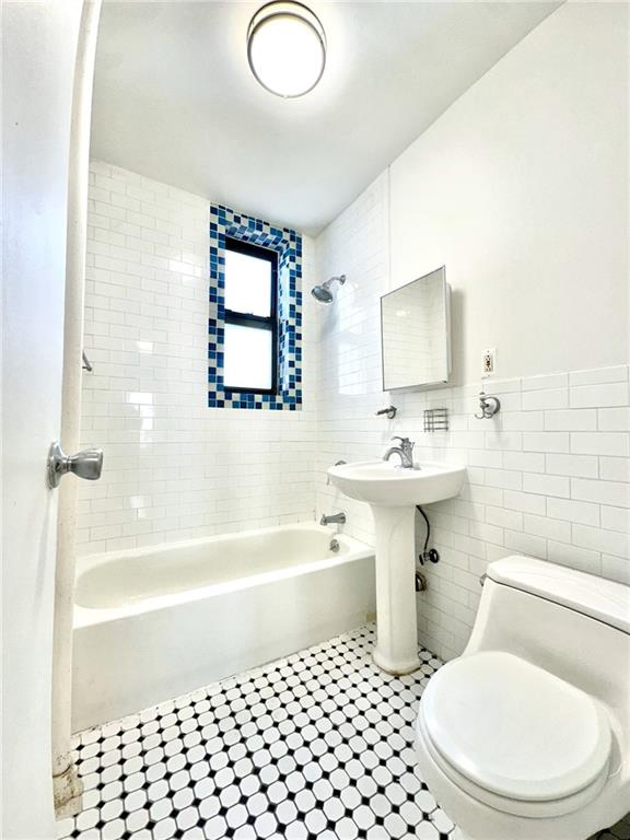 bathroom with a wainscoted wall, toilet, tile walls, and bathing tub / shower combination