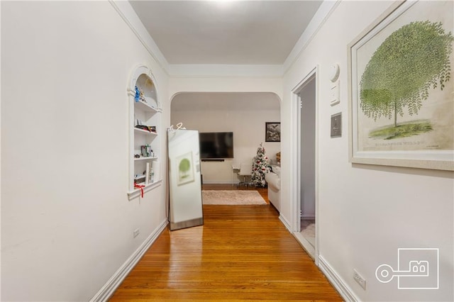 corridor featuring crown molding, light wood-type flooring, baseboards, and arched walkways
