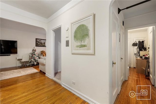 hallway with arched walkways, light wood-type flooring, and baseboards
