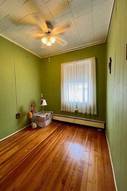 interior space featuring a baseboard radiator, a ceiling fan, baseboards, ornamental molding, and hardwood / wood-style floors