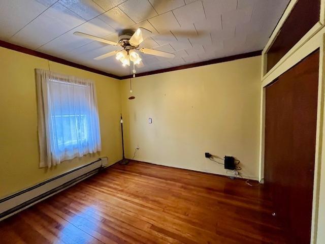 spare room with ceiling fan, ornamental molding, baseboard heating, and wood finished floors