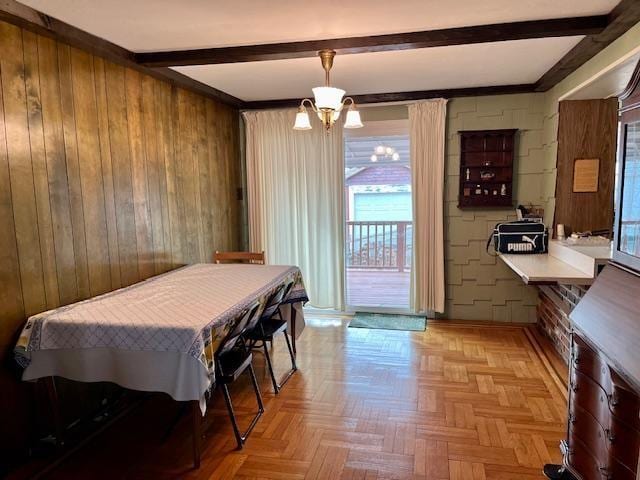 dining room featuring wood walls, a chandelier, and beam ceiling