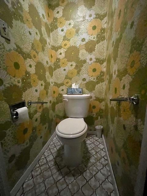 half bath with baseboards, toilet, and wallpapered walls