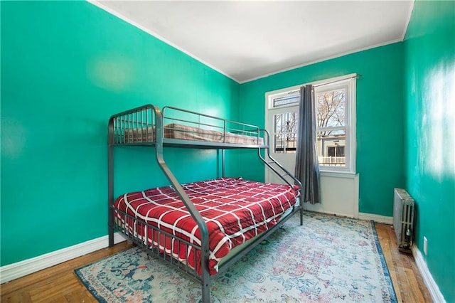 bedroom with radiator heating unit, wood finished floors, and baseboards