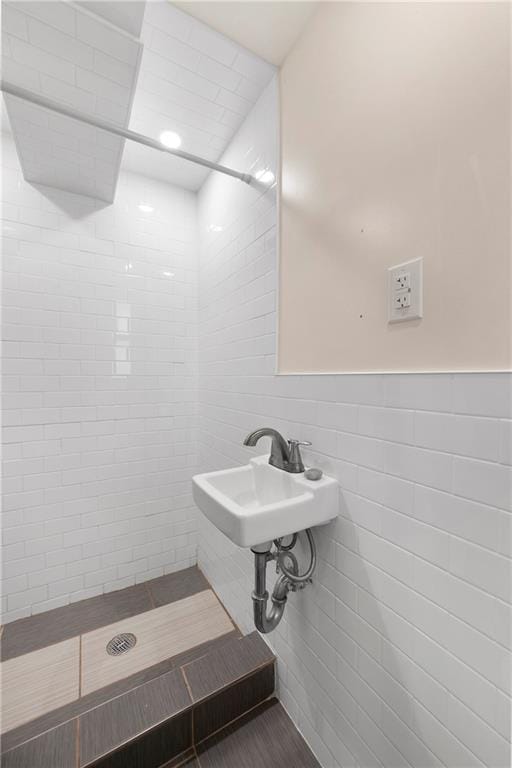 bathroom featuring wainscoting, a tile shower, tile walls, and a sink