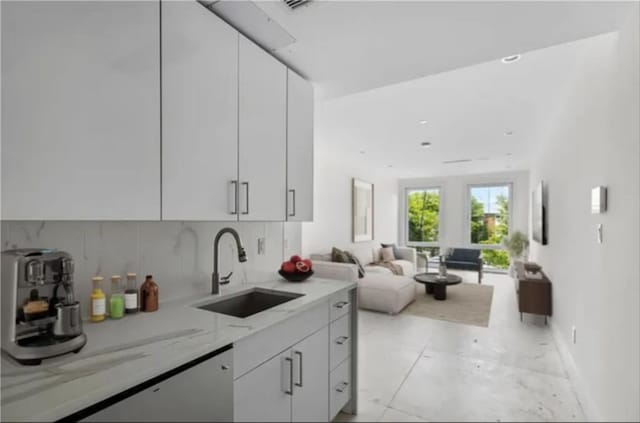 kitchen with tasteful backsplash, white cabinetry, light stone countertops, and sink