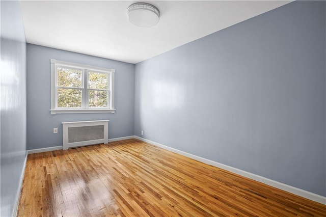 empty room featuring radiator, wood finished floors, and baseboards