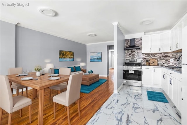 kitchen with wall chimney exhaust hood, gas stove, white cabinetry, crown molding, and backsplash