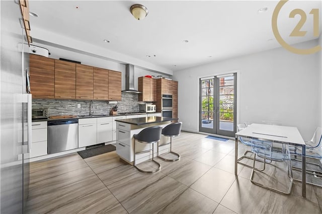 kitchen with white cabinets, appliances with stainless steel finishes, brown cabinets, wall chimney exhaust hood, and dark countertops