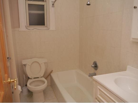 full bathroom featuring tile patterned floors, toilet, tiled shower / bath, tile walls, and vanity