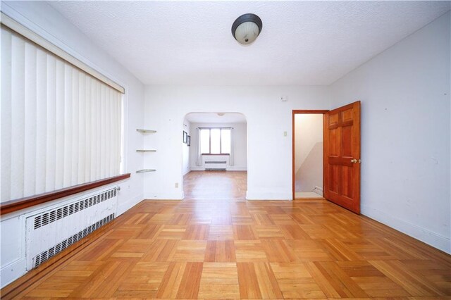 corridor featuring light parquet flooring, radiator heating unit, and a textured ceiling