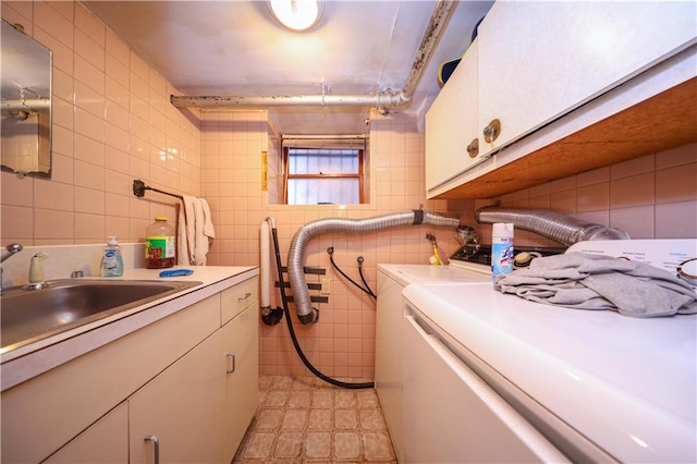 laundry area featuring a sink, cabinet space, tile walls, and washing machine and clothes dryer