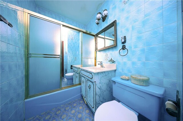 full bathroom with combined bath / shower with glass door, tile walls, vanity, toilet, and tile patterned floors