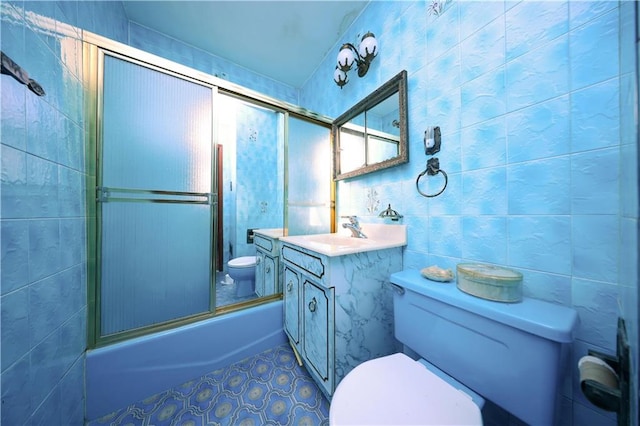 full bath with toilet, shower / bath combination with glass door, tile patterned flooring, vanity, and tile walls