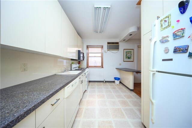 kitchen with light tile patterned flooring, an AC wall unit, sink, white cabinets, and white appliances