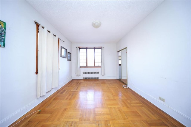 empty room with a textured ceiling, radiator heating unit, and baseboards