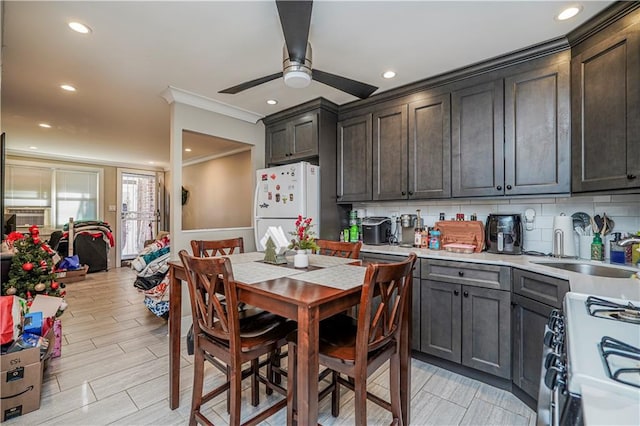 kitchen with a sink, backsplash, gas range oven, freestanding refrigerator, and light countertops