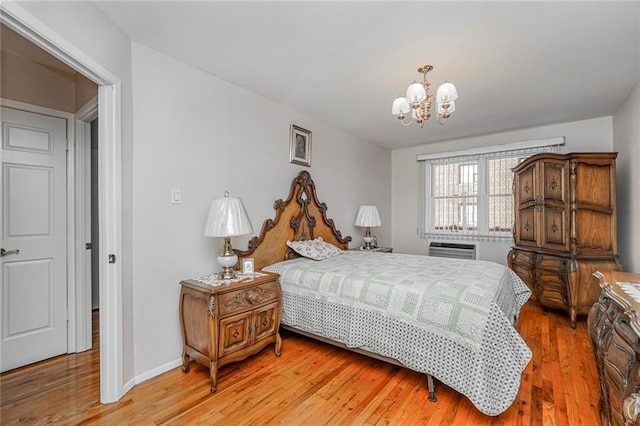 bedroom featuring a wall unit AC, a notable chandelier, baseboards, and light wood-type flooring