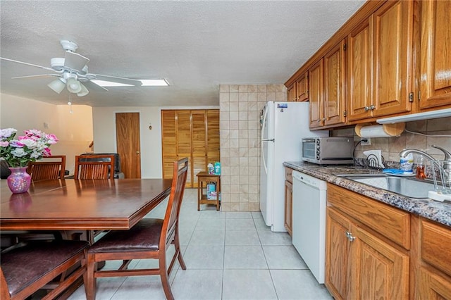 kitchen featuring light tile patterned floors, brown cabinetry, white appliances, a textured ceiling, and a sink