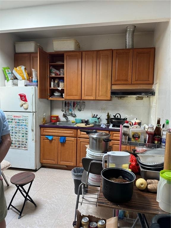 kitchen with light tile patterned flooring, decorative backsplash, sink, and white fridge