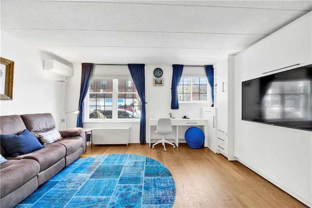 living area with a textured ceiling, wood finished floors, built in desk, and a wall mounted air conditioner