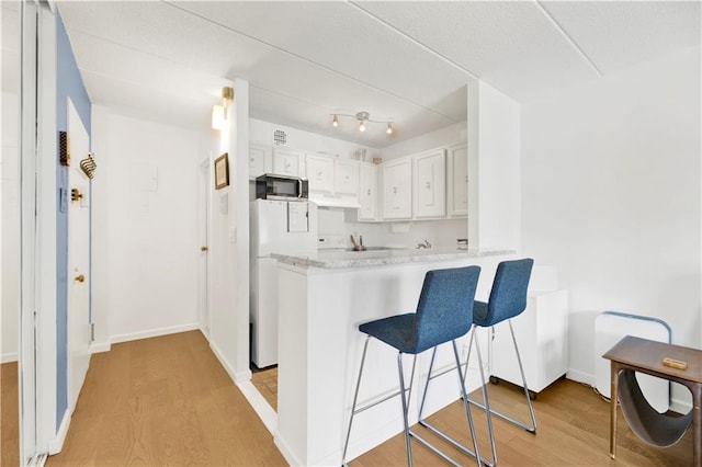 kitchen with stainless steel microwave, light wood-style flooring, freestanding refrigerator, white cabinets, and under cabinet range hood