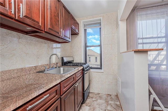 kitchen featuring visible vents, a sink, light stone counters, tile walls, and stainless steel gas range