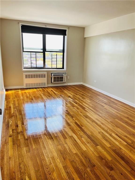 unfurnished room featuring hardwood / wood-style flooring, an AC wall unit, and radiator