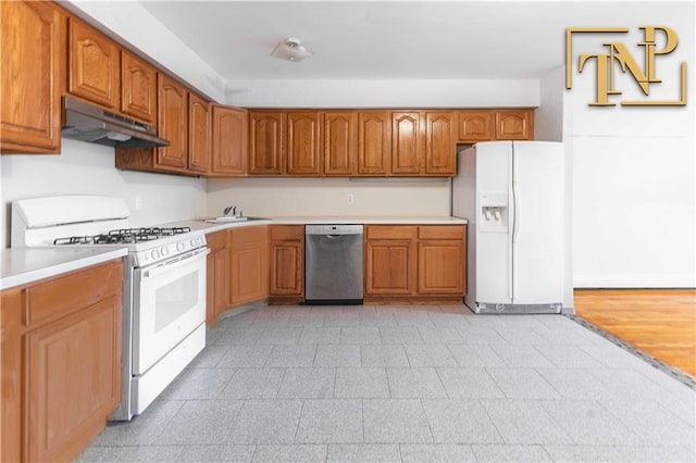 kitchen with under cabinet range hood, light countertops, brown cabinetry, white appliances, and a sink