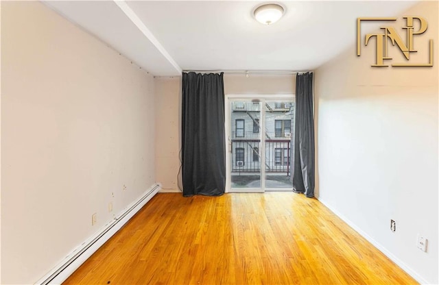 unfurnished room with a baseboard heating unit, baseboards, and wood finished floors