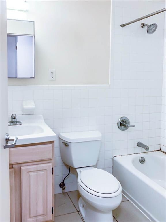 full bathroom featuring tile walls, tiled shower / bath combo, vanity, tile patterned floors, and toilet