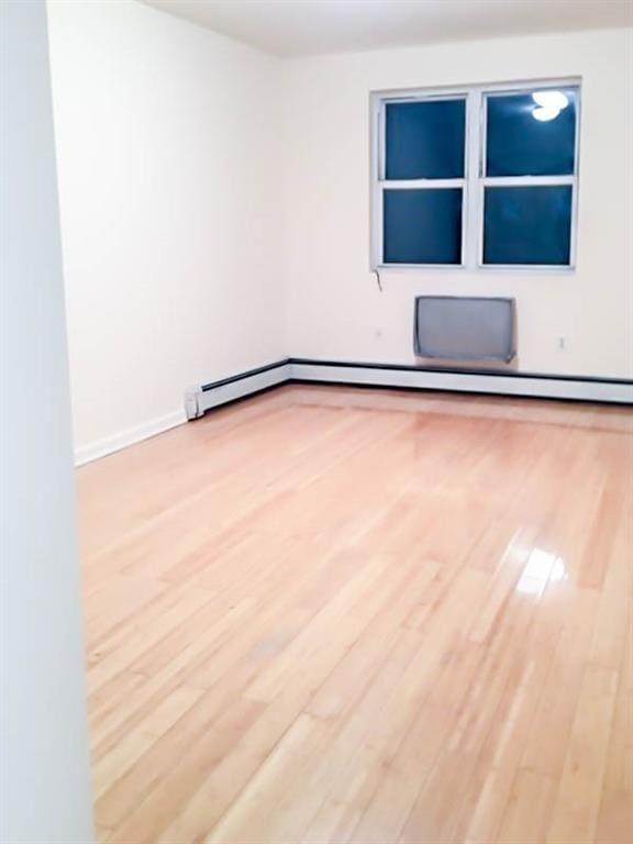 empty room with baseboard heating and light wood-type flooring