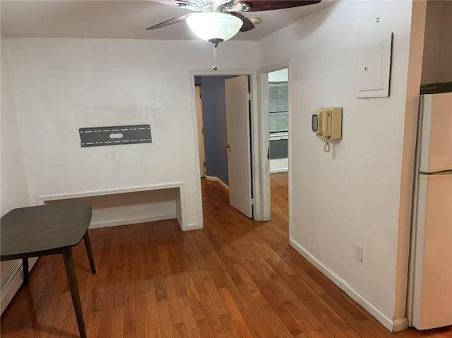 corridor with a baseboard heating unit, hardwood / wood-style flooring, and electric panel