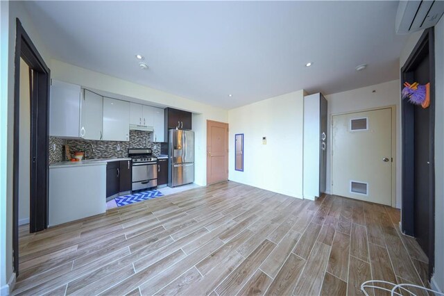 kitchen with white cabinetry, tasteful backsplash, a wall mounted AC, stainless steel appliances, and light hardwood / wood-style floors