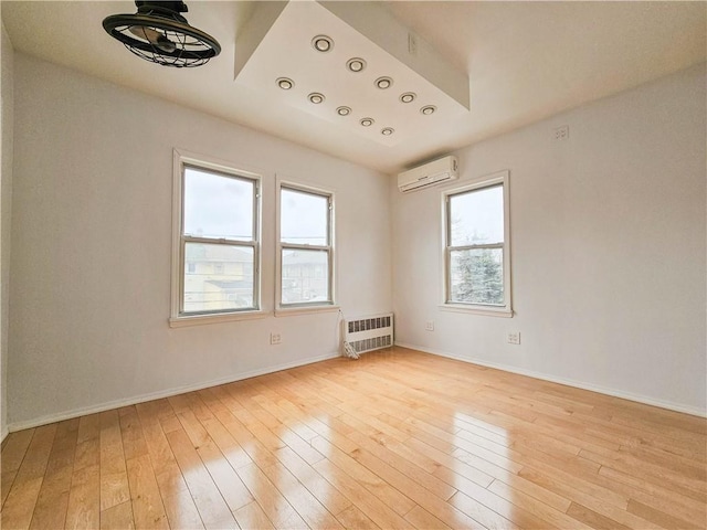 unfurnished room featuring a wall unit AC, light wood-style floors, and baseboards