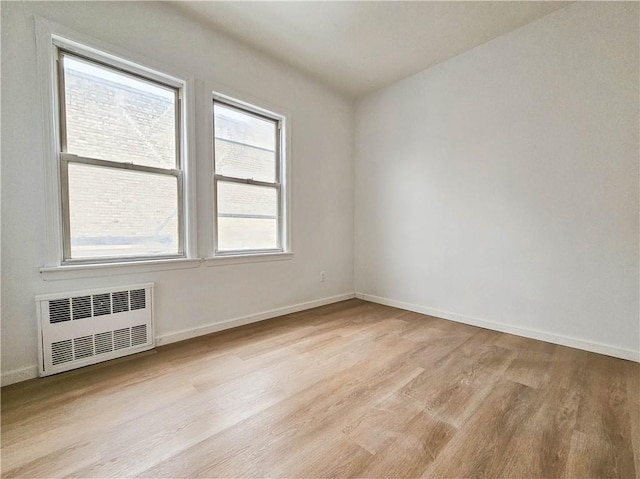 spare room with radiator, light wood-style flooring, and baseboards