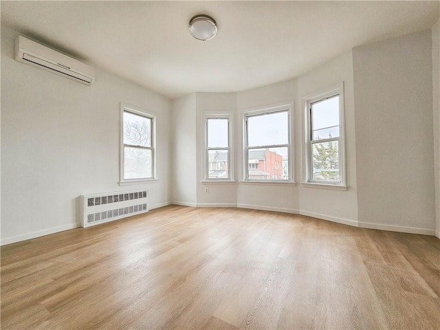 unfurnished room featuring radiator, a wall unit AC, baseboards, and light wood finished floors