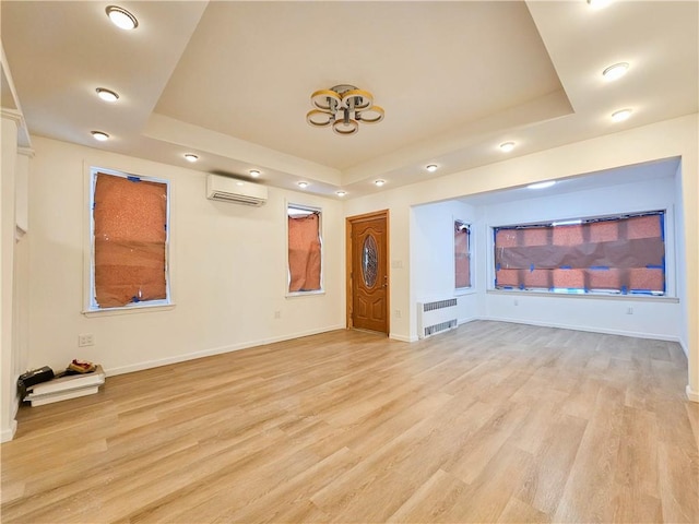 unfurnished living room featuring radiator heating unit, a tray ceiling, light wood-style flooring, and an AC wall unit