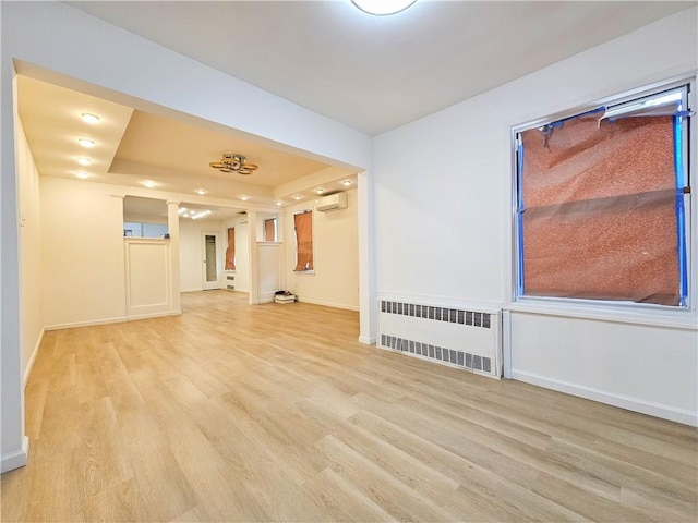 spare room with a tray ceiling, baseboards, radiator heating unit, light wood-style floors, and ornate columns