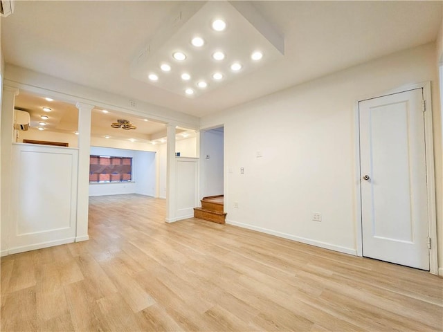 spare room featuring decorative columns, baseboards, a raised ceiling, stairs, and light wood-type flooring