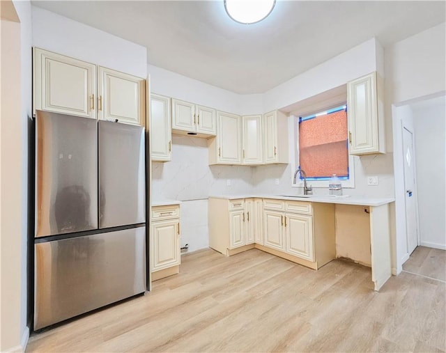 kitchen featuring light countertops, decorative backsplash, freestanding refrigerator, a sink, and light wood-type flooring