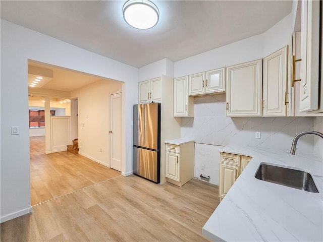 kitchen featuring light stone counters, a sink, light wood-type flooring, freestanding refrigerator, and decorative backsplash