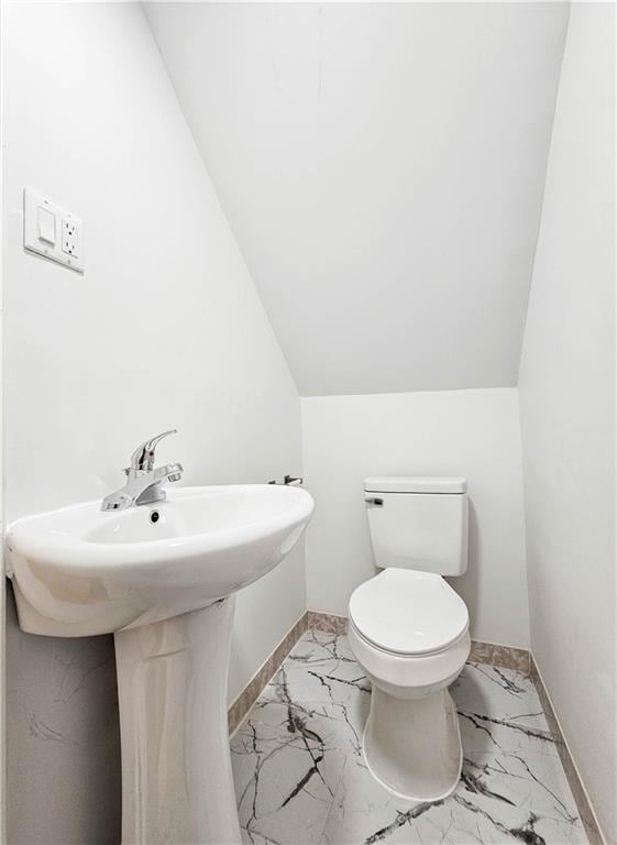 half bathroom featuring toilet, marble finish floor, baseboards, and vaulted ceiling