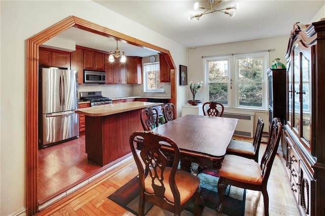 dining area with radiator, pendant lighting, a center island, an inviting chandelier, and light parquet floors