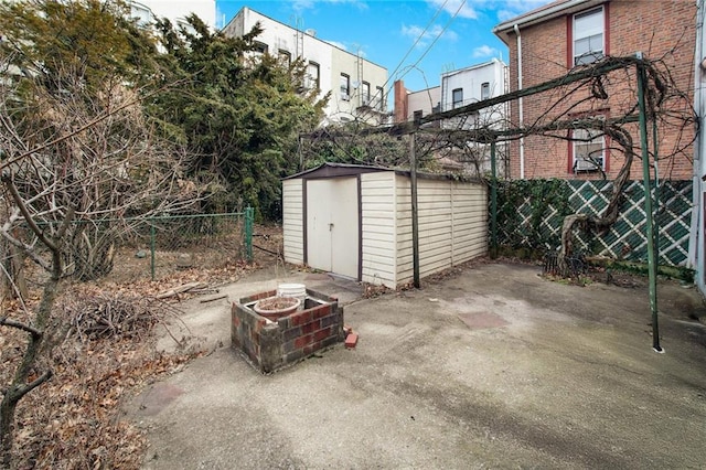 view of patio / terrace featuring a storage unit, an outdoor fire pit, an outbuilding, and fence