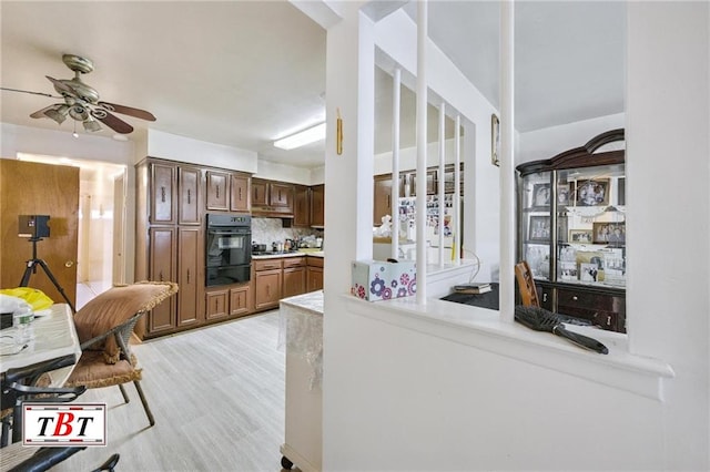 kitchen featuring dobule oven black, tasteful backsplash, light wood-style floors, light countertops, and ceiling fan